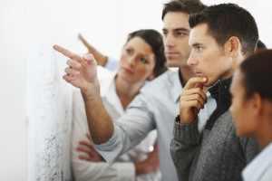 Group of business associates looking and pointing at a chart put up on the wall